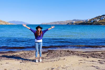 Rear view of woman with arms raised on beach against blue sky