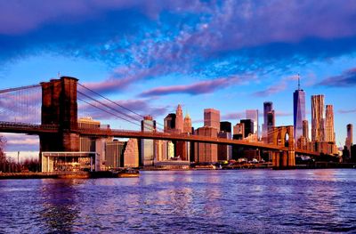 Bridge over river by buildings in city against sky