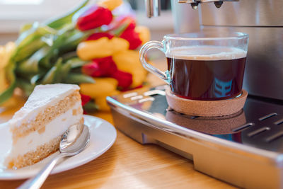 Cup of coffee with milk, piece of cake and tulips flowers on wooden kitchen table. freshly brewed 