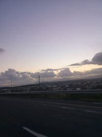 Road by city against sky during sunset