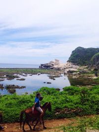 Rear view of man riding horse on sea shore against sky