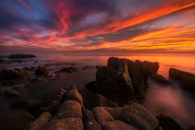 Rocks by sea against romantic sky at sunset