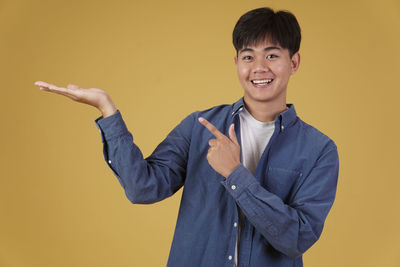 Portrait of young man standing against yellow background