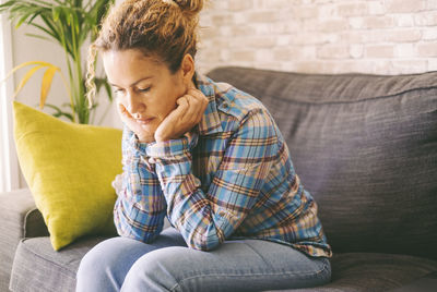 Young woman using phone while sitting on sofa at home