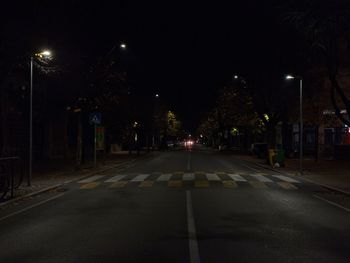 Empty road along illuminated street lights at night