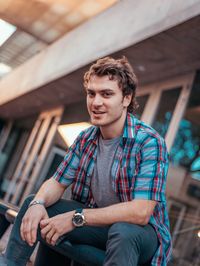 Portrait of smiling young man sitting on railing