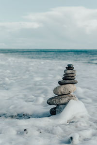 Stack of pebbles in sea against sky during winter