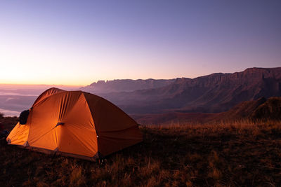 Tent on field by mountains against sky during sunset