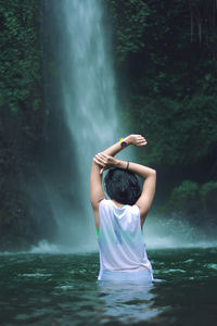 Rear view of woman standing in river against waterfall