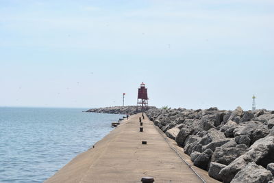 Lighthouse on pier over sea against sky