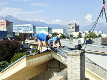 Workers installing wooden plank on rooftop of house