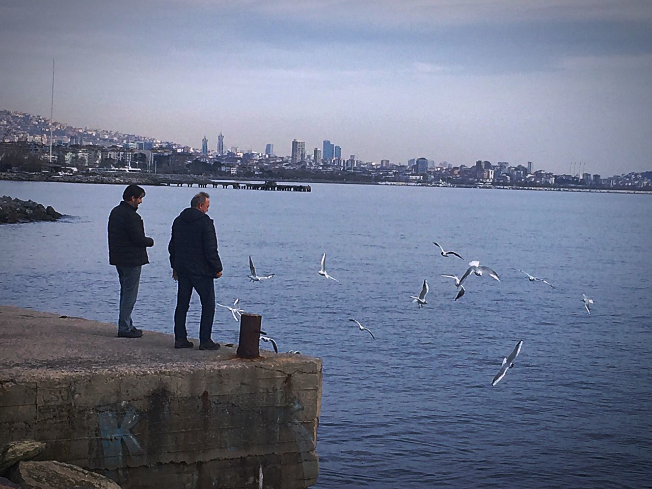 REAR VIEW OF PEOPLE ON SEA SHORE AGAINST SKY