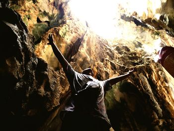 Low angle view of teenage boy with arms raised standing against rock