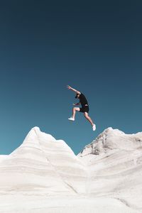 Low angle view of man jumping on mountain against sky