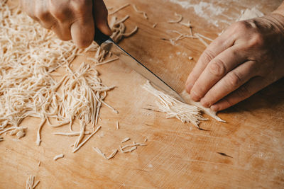 A woman cuts the dough with a knife and makes homemade noodles in the kitchen.