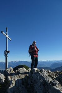 Low angle view of man standing on rock against clear blue sky