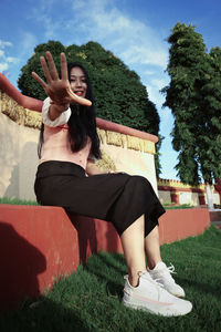 Full length of young woman sitting on grass against trees