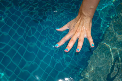 Cropped hand of woman touching water in swimming pool