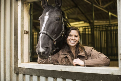 Portrait of happy young woman with horse in stable