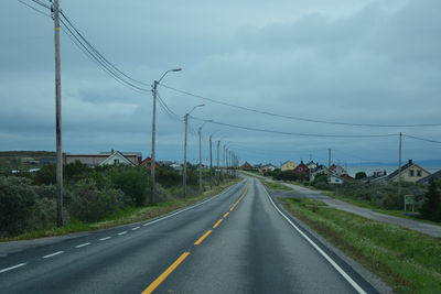 Road by electricity pylon against sky