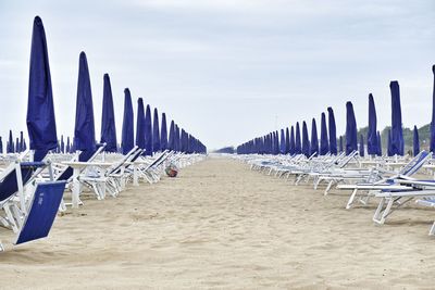 Parasols and lounge chairs arranged at beach against sky