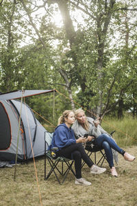 Full length of woman talking to daughter while sitting at campsite