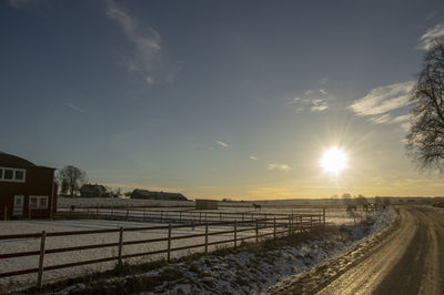 Road by snow field against sky during sunset