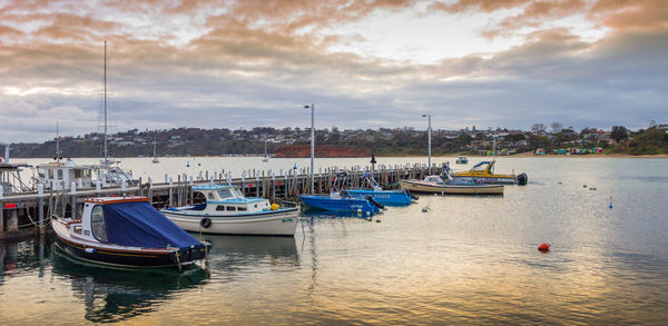 Boats moored in harbor at sunset