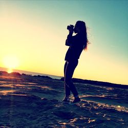 Woman standing at beach against clear sky during sunset