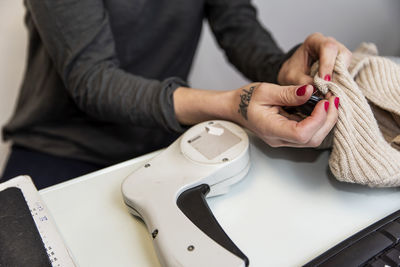 Midsection of woman scanning clothes while sitting at table in store