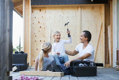 Happy parents with daughter holding hammer while sitting outside house