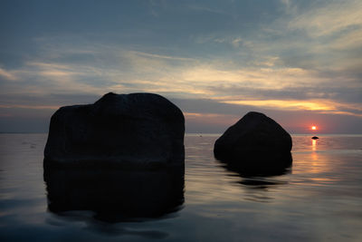 Rocks in sea against sky during sunset