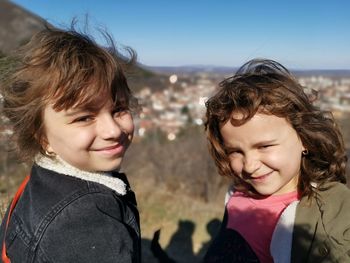 Portrait of smiling sisters standing against sky