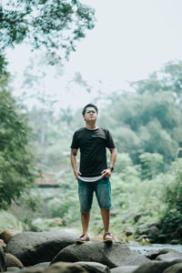 Full length of young man standing on rock in forest