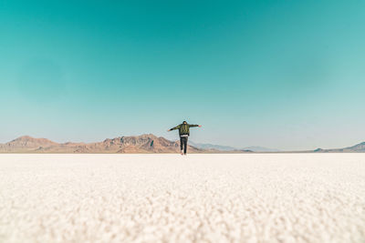 Surface level image of man with arms outstretched walking on land against clear sky
