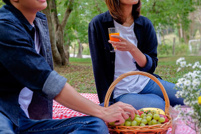 Midsection of friends having fruits and juice at park