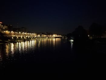 Illuminated city by river against clear sky at night