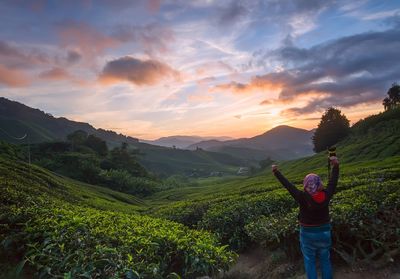 Man standing on green landscape against sky during sunset
