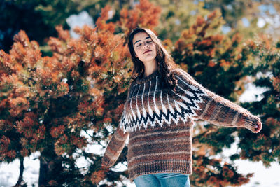 Young woman with arms outstretched arms outstretched standing against trees during winter