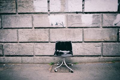 Abandoned chair on footpath against concrete wall