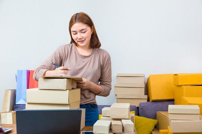 Young woman writing on clipboard while sitting by boxes