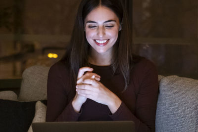 Young woman using phone while sitting on sofa at home