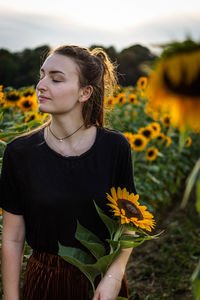 Young woman holding sunflower while standing outdoors