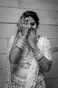 Portrait of woman holding camera while standing against wall