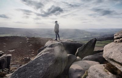 Rear view of man standing on rocks against sky