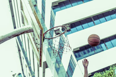 Cropped hand throwing ball in basket against building in city