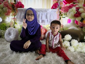 Portrait of siblings sitting on carpet by flowers