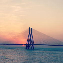 Suspension bridge over sea against sky during sunset