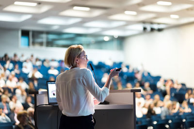 Female speaker giving a talk on corporate business conference. unrecognizable people in audience at