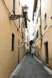 Rear view of man walking on narrow street amidst buildings